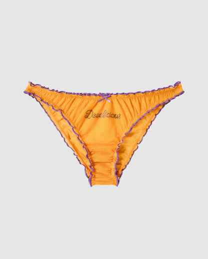 An ruffled mesh bikini brief in a mustard orange with lilac accessories.